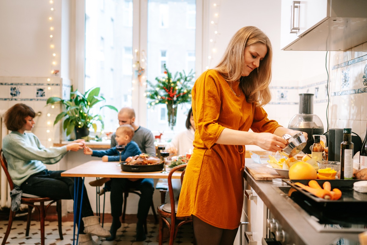 Eine Frau bereitet in einer Küche Essen zu, während eine Familie am Tisch sitzt.