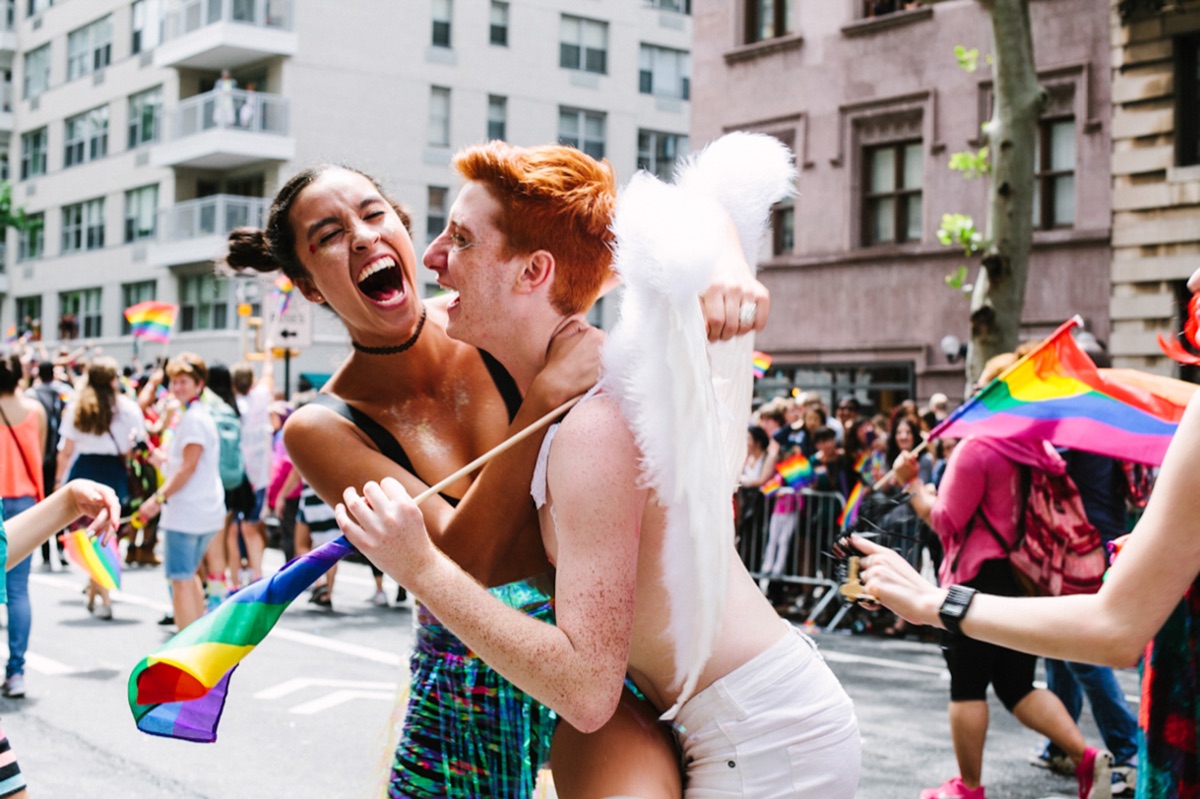 Zwei junge Menschen liegen sich lachend bei einer Pride-Parade in den Armen.