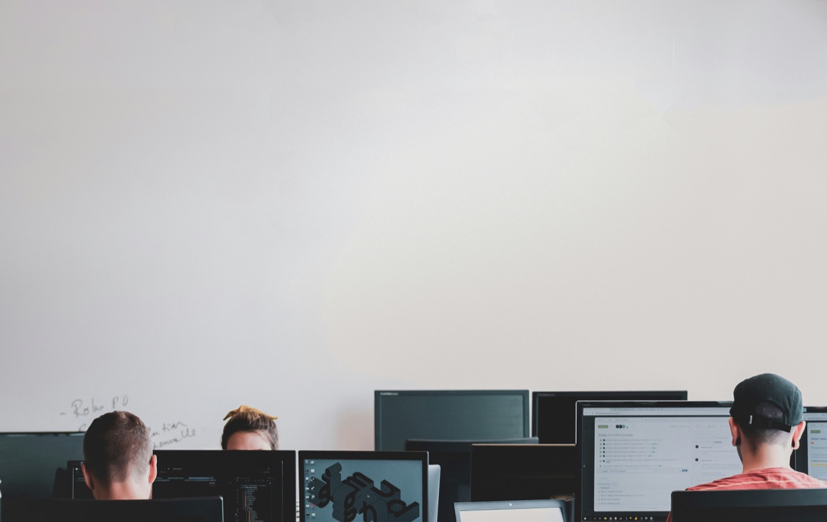 Menschen arbeiten an mehreren Computerbildschirmen in einem Büro.